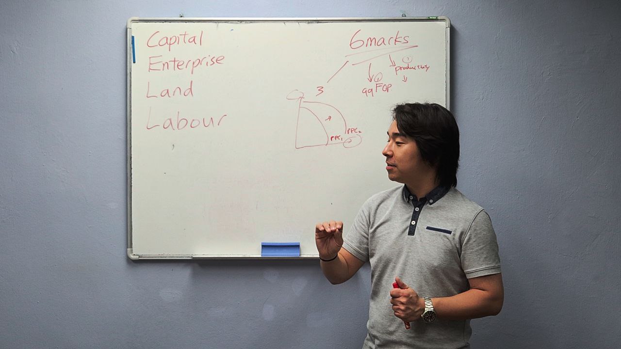 Kirby Ng teaching economics at the whiteboard — structured essays and evaluation in action